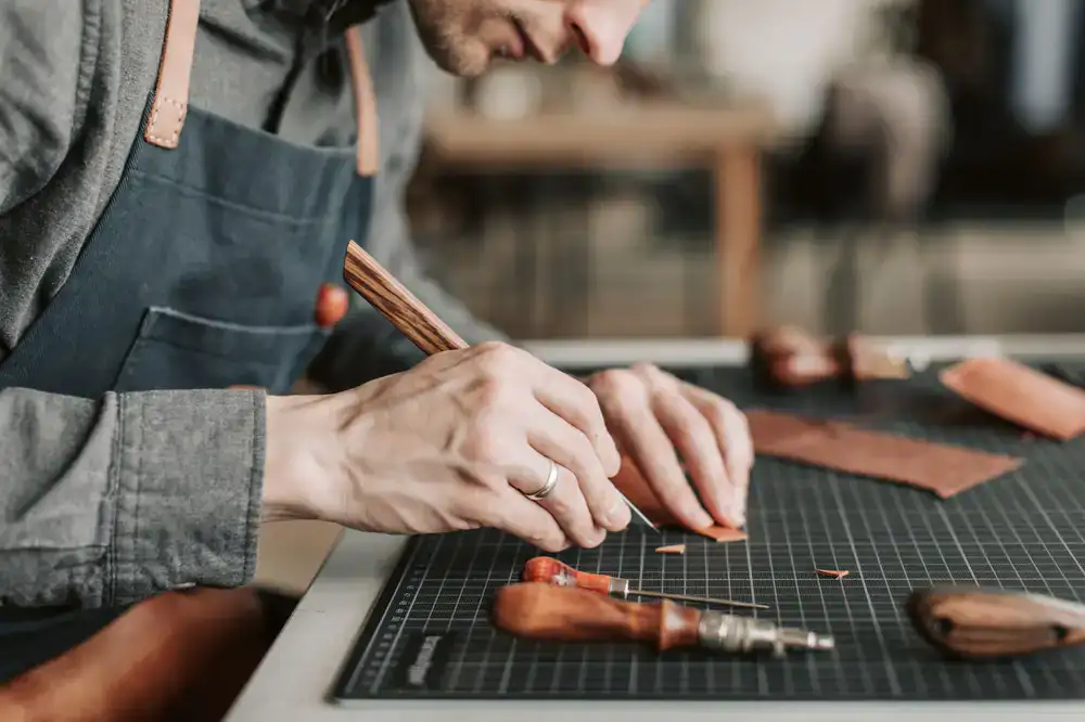 A craftsman's hands working on a leather piece at a sturdy wooden bench